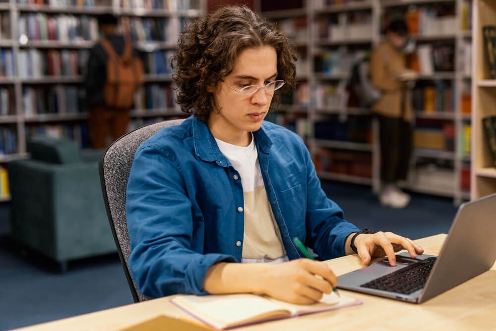 boy-studying-in-the-university-library (1) estudante de um curso de graduação na biblioteca, lendo